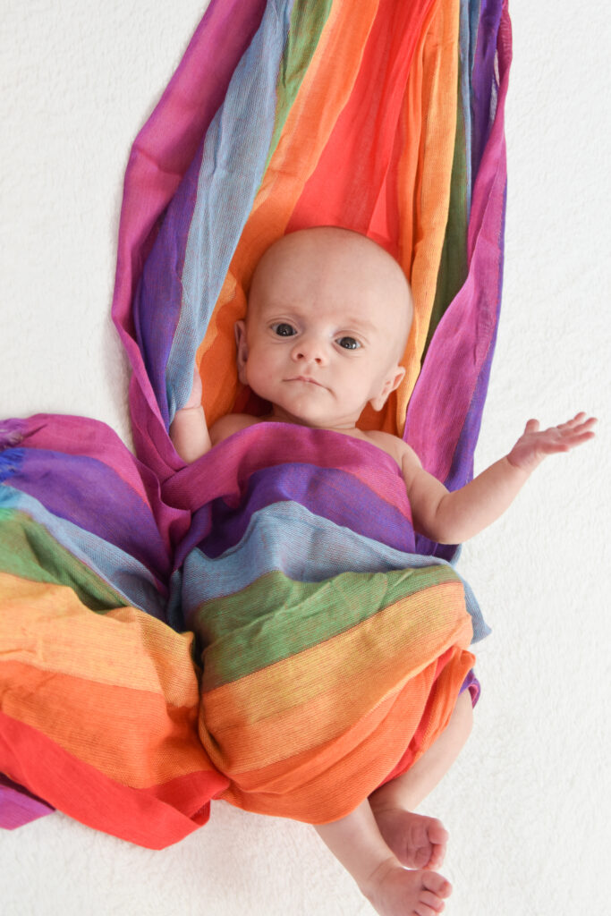 Little Jo in ein Tuch in Regenbogenfarben eingewickelt